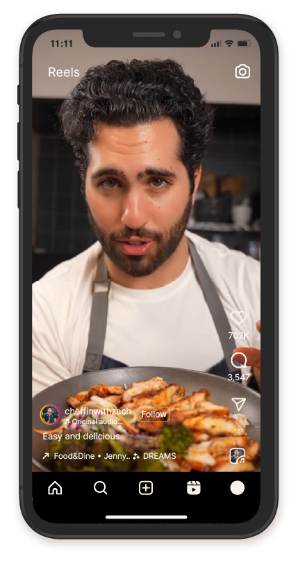 A person wearing an apron presents a plate of grilled food in a cooking video displayed on a smartphone screen.